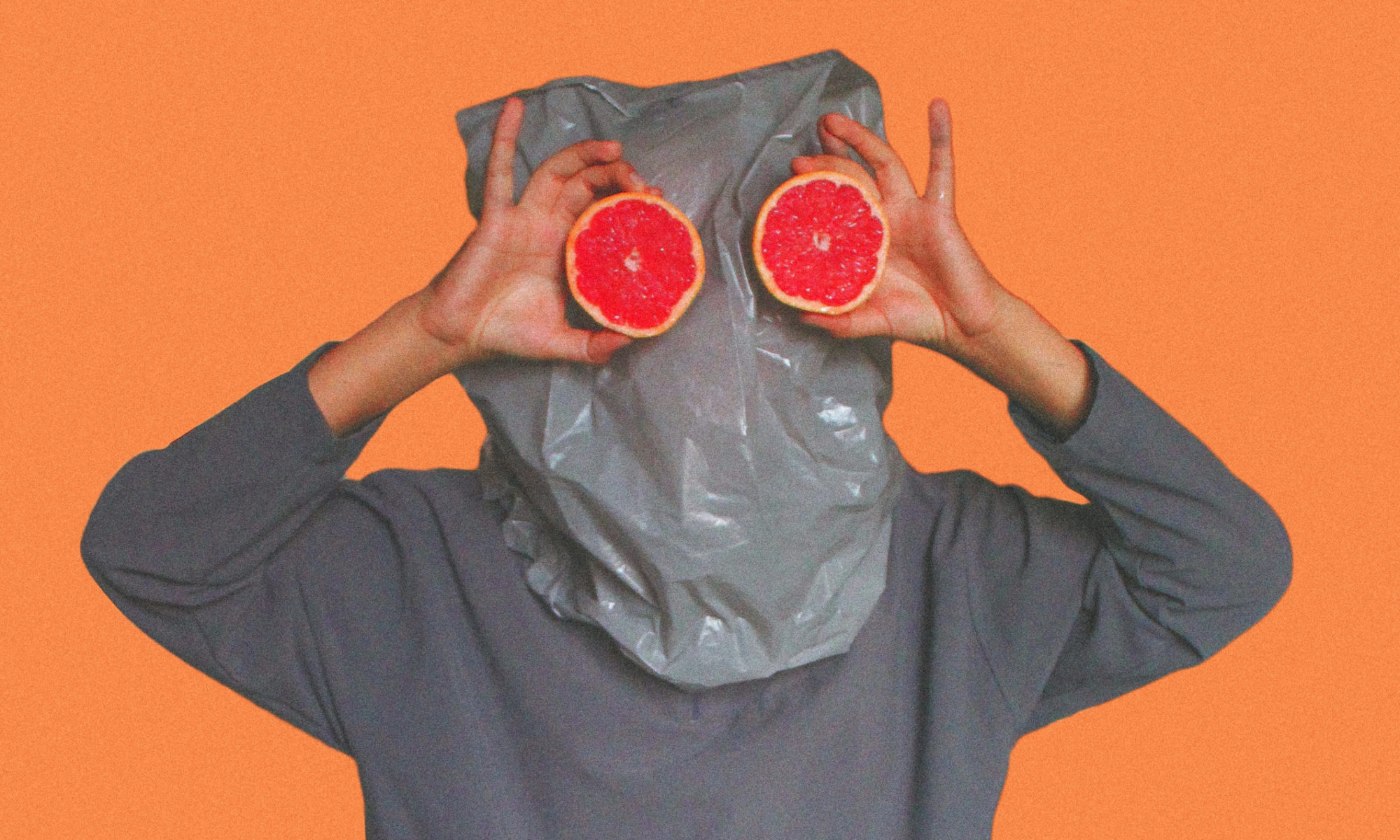 Person covered with plastic bag on head while holding sliced blood orange