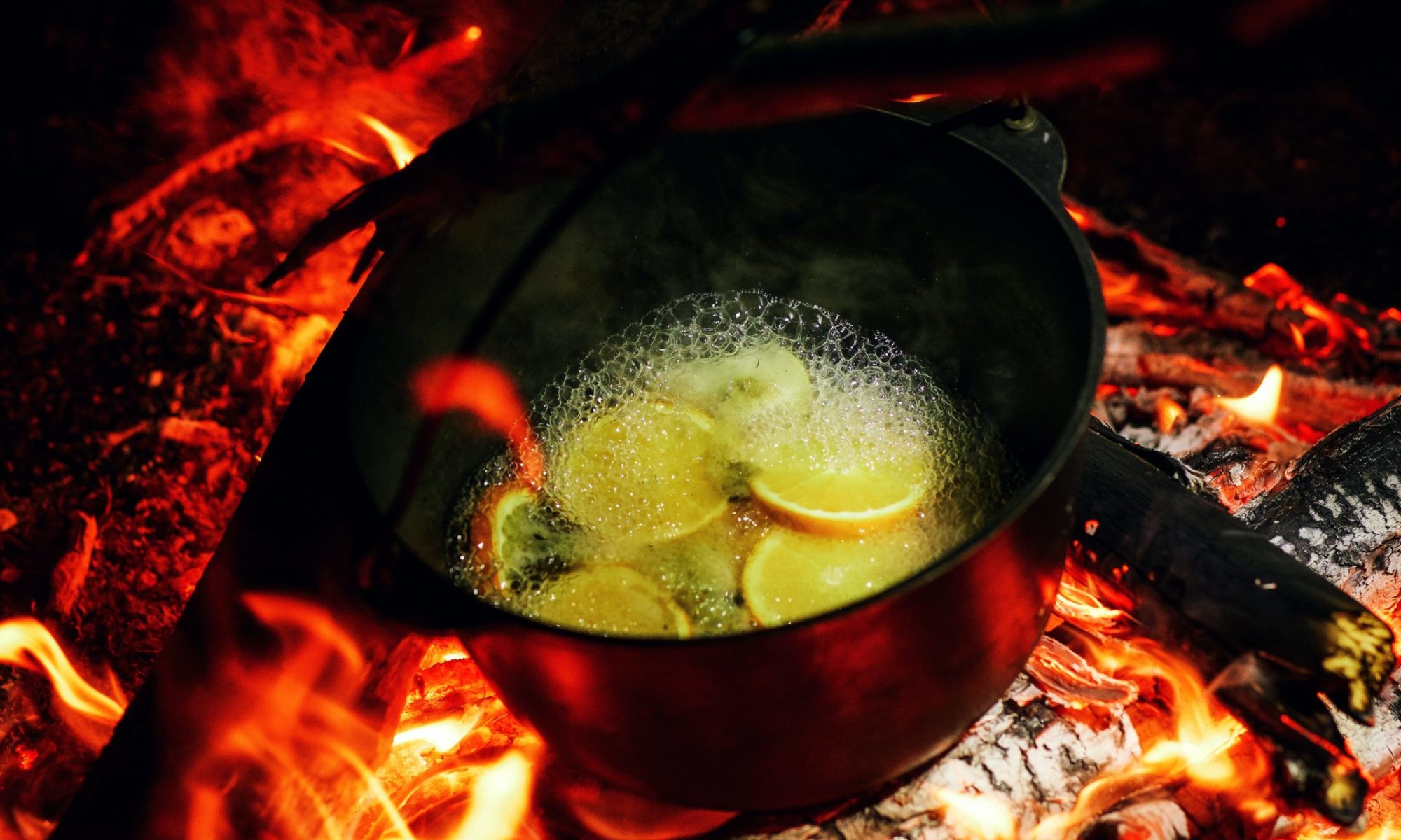 The cauldron is boiling on the coals of the fire. In a camping boiler on a halt, mulled wine with lemon and spices is cooked.