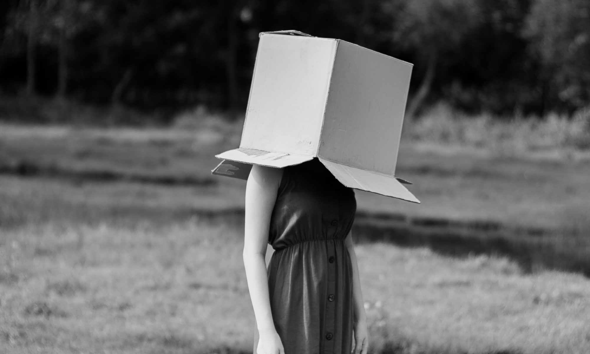 Faceless woman with cardboard box on head against pond