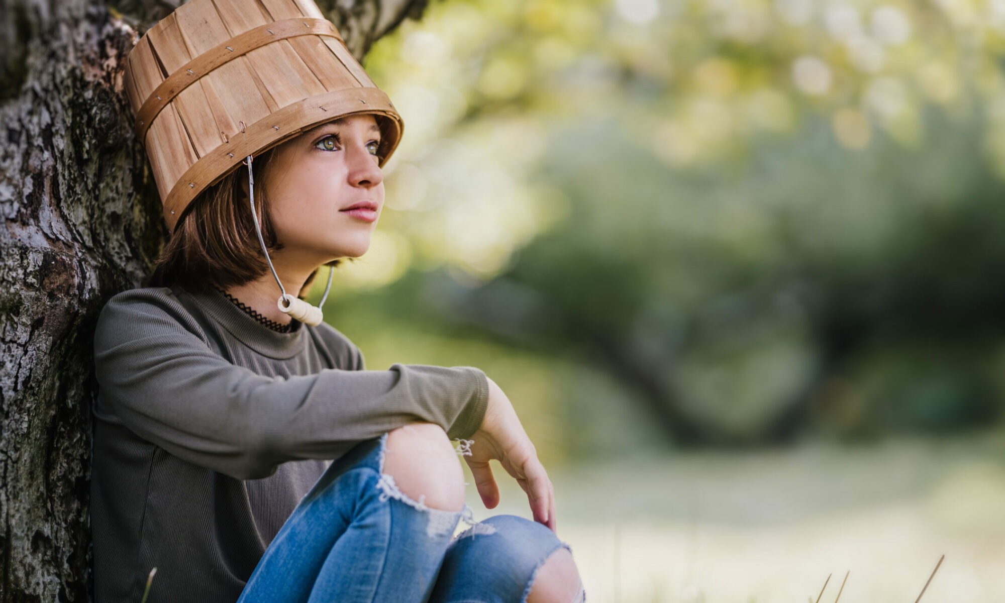 Funny girl with bucket on head sitting in forest