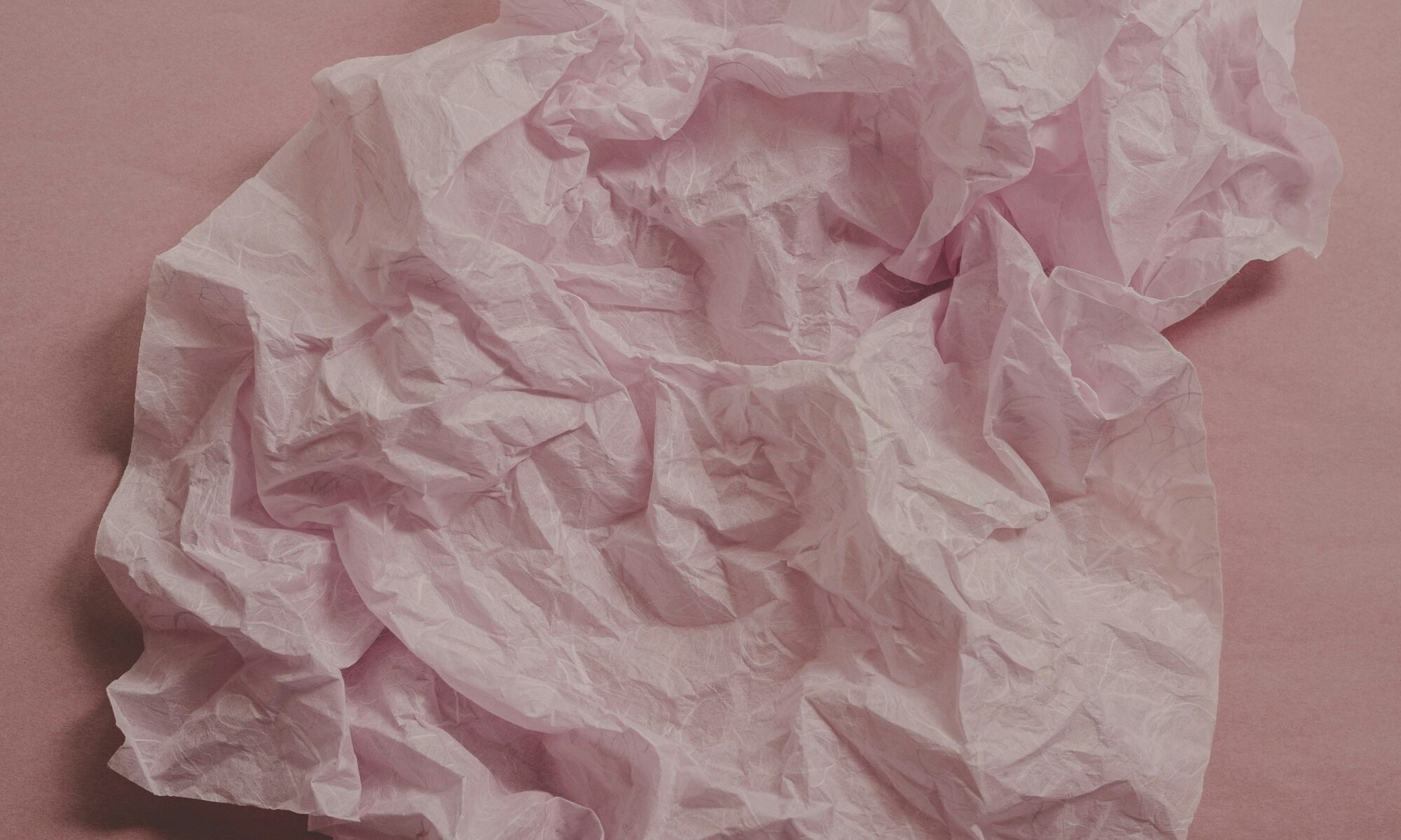 flat lay of wrinkled pink mulberry silk paper on a dusty pink paper background captured with natural backlighting